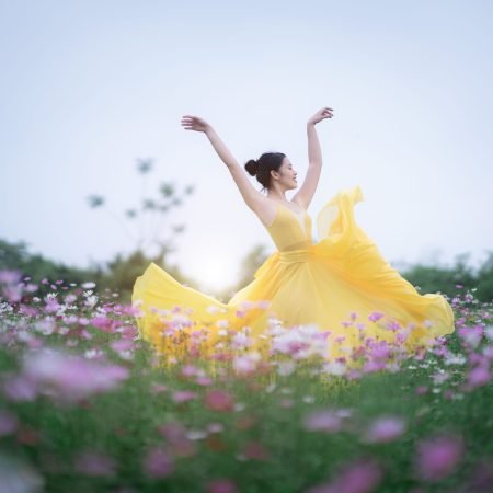 Donna in abito giallo che danza libera in un prato fiorito
