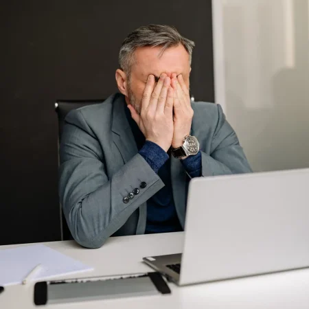 Uomo in abito formale che si copre il volto al computer